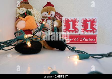 Calendrier à rebours de onze jours jusqu'à Noël composé de blocs de bois sur un manteau avec des lumières et un bonhomme de neige en peluche. Banque D'Images