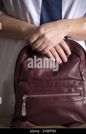 Les mains d'une femme médecin en uniforme sur un sac à dos en cuir bordeaux. Banque D'Images