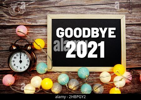 Au revoir 2021 texte sur tableau noir en bois avec réveil et décoration de boules de coton LED sur fond de bois Banque D'Images
