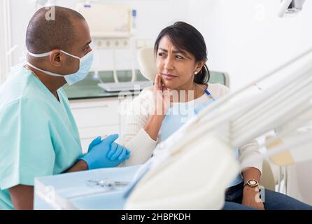 Latina souffrant de maux de dents parlant au stomatologiste tout en étant assis sur une chaise dentaire dans la clinique Banque D'Images