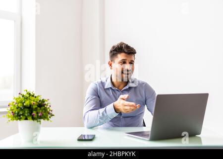 Jeune homme d'affaires concentré dans les lunettes portant des écouteurs, tenant des appels vidéo avec des clients sur ordinateur portable. Banque D'Images