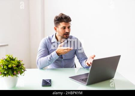 Jeune homme d'affaires concentré dans les lunettes portant des écouteurs, tenant des appels vidéo avec des clients sur ordinateur portable. Banque D'Images