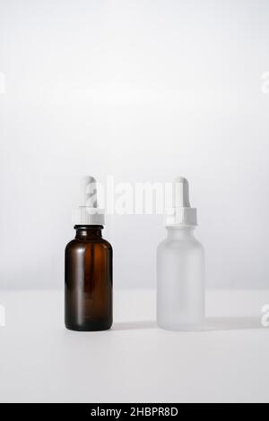 flacons de sérum en verre blanc mat et marron avec compte-gouttes sur fond blanc clair.Liquide facial anti-âge avec peptides et collagène Banque D'Images