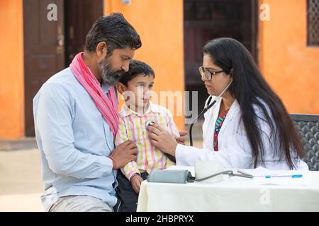 Femme indienne médecin avec stéthoscope vérifiant le rythme cardiaque ou la respiration du petit patient enfant au village, Kid avec son père se faire examiner par PE médical Banque D'Images