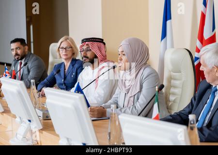 Jeune femme musulmane déléguée dans le hijab faisant rapport à des collègues étrangers lors d'un sommet ou d'un forum politique Banque D'Images