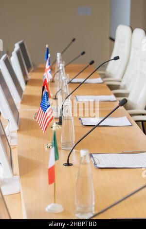 Rangée de bouteilles avec eau, drapeaux nationaux, microphones, moniteurs d'ordinateur et papiers sur table longue dans la salle de conférence Banque D'Images