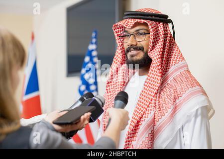 Jeune homme d'affaires arabe vêque de vêtements nationaux, qui donne une interview aux journalistes après un événement politique dans la salle de conférence Banque D'Images