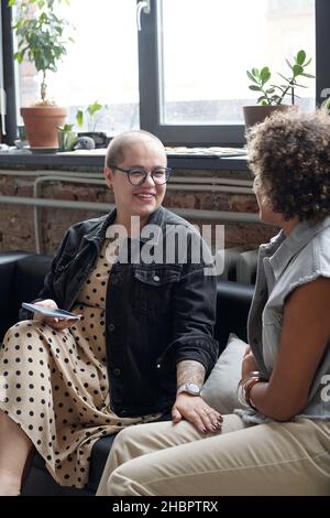 Bonne jeune femme d'affaires caucasienne avec un téléphone portable parlant à son collègue biracial lors d'une réunion de travail Banque D'Images