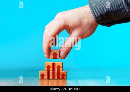 Le concept de l'amélioration des affaires, du développement personnel et de la croissance.La main d'un homme met un cube avec une flèche sur le dessus de la pyramide.Fond bleu Banque D'Images