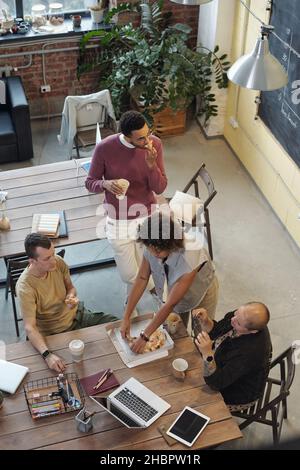 Quatre jeunes collègues se sont réunis à table pour la pause déjeuner, manger de la pizza et prendre des boissons et communiquer entre eux Banque D'Images