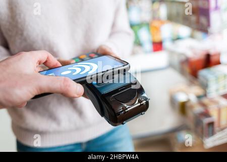 Le vendeur possède un terminal de paiement, et l'homme paie pour l'achat en ligne à l'aide d'un smartphone.Sur l'écran du téléphone, réseau wi-fi.Concept NFC, bus Banque D'Images