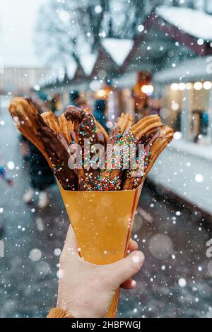 Gaufres churos dans la main sur le marché de la neige d'hiver.Churros cuisine mexicaine de rue dessert.Bonbons fast-food, biscuits de Noël.Photo de haute qualité Banque D'Images