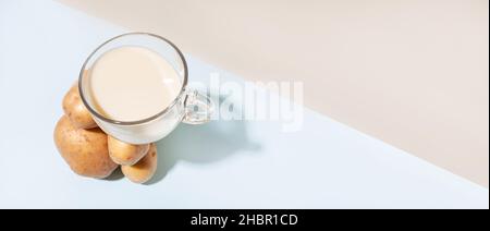 Lait de remplacement.Composition moderne avec une tasse de lait de pomme de terre qui équilibre sur un tas de pommes de terre. Banque D'Images