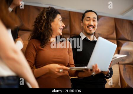 Bonne femme d'affaires discutant avec des collègues masculins et féminins au bureau sur ordinateur portable Banque D'Images