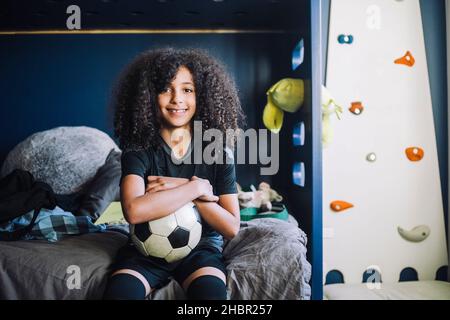 Portrait d'une fille avec ballon de football assis sur le lit dans la chambre Banque D'Images