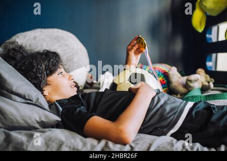 Fille regardant la médaille en étant couché sur le lit dans la chambre Banque D'Images