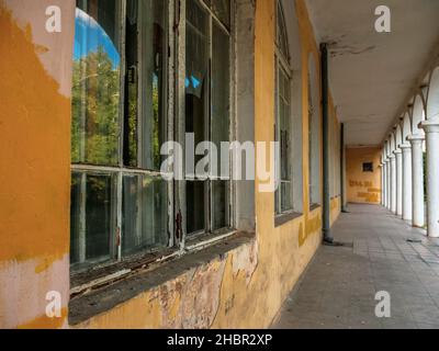 Long passage le long de l'ancien bâtiment abandonné avec de hautes fenêtres à la française avec des lunettes cassées. Banque D'Images