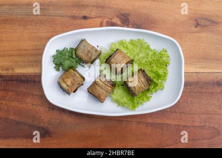 Rouleaux d'aubergines décorés de laitue fraîche et de persil sur une assiette blanche, fond en bois.Vue de dessus, gros plan avec espace copie, cuisine géorgienne. Banque D'Images