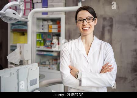 Portrait d'une jeune femme dentiste sur le fond de la clinique.Le dentiste est debout avec ses bras croisés, regardant la caméra et souriant. Banque D'Images