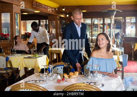 Gentilhomme aidant jeune femme attrayante avec sa chaise dans le restaurant Banque D'Images