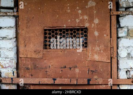 Un fragment d'une vieille porte en métal rouillé avec une fenêtre en treillis Banque D'Images