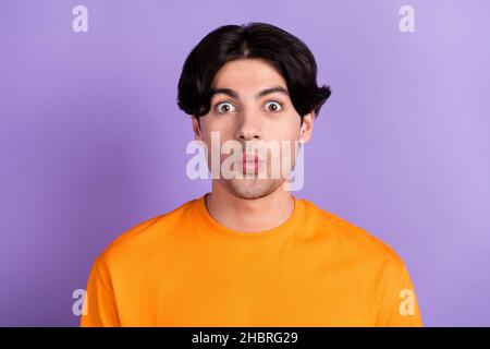 Photo de jeune heureux drôle funky stupéfié visage choqué bonne humeur porter t-shirt orange isolé sur fond violet de couleur Banque D'Images