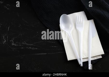 Appareils en plastique sur fond noir.Cuillères blanches, fourchette et couteau sur une serviette de table vue de dessus.Appareils de cuisine en plastique avec place pour le texte. Banque D'Images