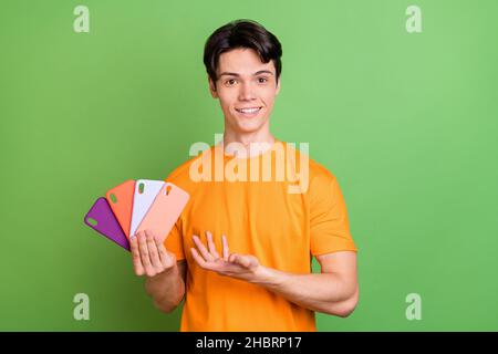 Photo de heureux gai jeune positif homme montrer les étuis de téléphone vente sourire isolé sur fond vert de couleur Banque D'Images