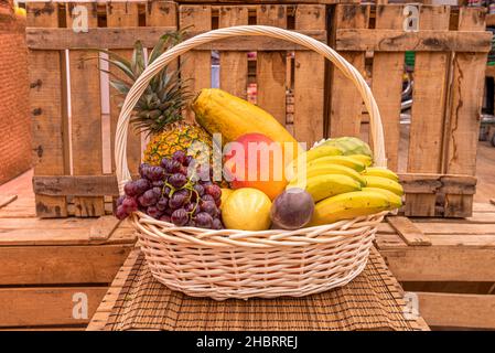 Panier en osier non verni rempli de fruits frais, de bananes, de mangue, de prunes et d'ananas Banque D'Images