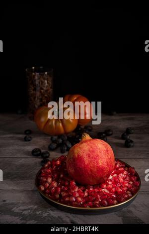 Encore la vie avec des grenades, des grains, des bleuets, des anis étoilé et des tomates roses sur une table en bois Banque D'Images