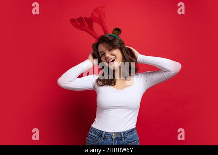 Studio photo de mignonne jolie jeune fille gaie portant des bois de cerf jouet ayant amusant isolé sur fond rouge. Banque D'Images