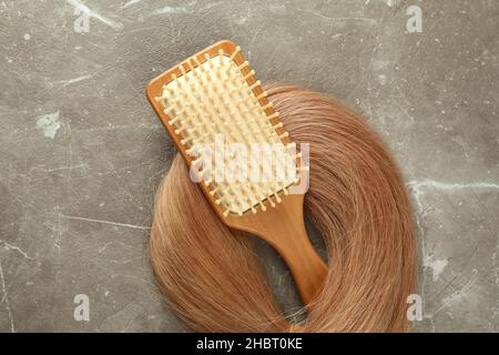 Une mèche de cheveux femelle avec brosse à cheveux sur fond texturé gris Banque D'Images