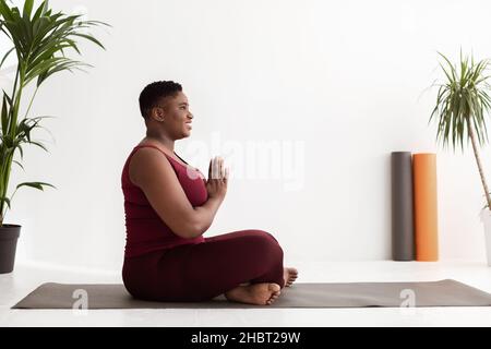 Vue latérale d'une femme noire chubby positive ayant un entraînement de yoga Banque D'Images
