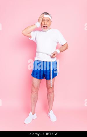 Pleine longueur taille de corps photo stupéfié homme aîné mesurant la taille avec le ruban a besoin de graisse régime isolé pastel couleur rose fond Banque D'Images