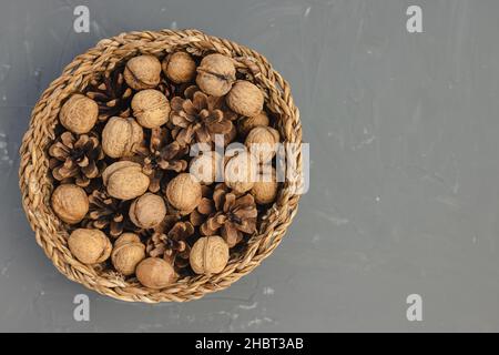 Noix crues en carapace et cônes de pin en panier comme décoration de table d'automne ou de Noël sur fond gris foncé.Vue de dessus, espace de copie Banque D'Images