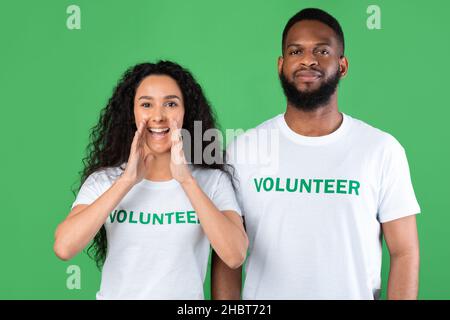 Deux volontaires criant Hey tenant les mains près de la bouche, fond vert Banque D'Images