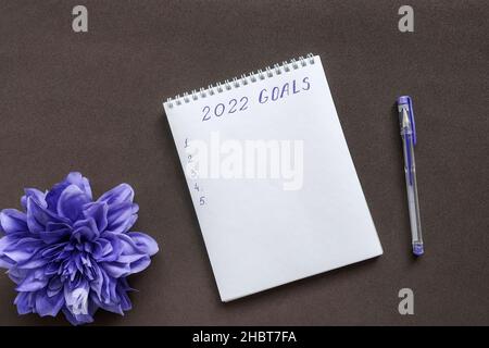 Vue du haut 2022 buts lettrage dans notebooka et fleur pourpre sur fond marron.Violet couleurs tendance 2022.Mise au point sélective. Banque D'Images