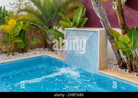 Vue rapprochée d'une cascade dans une piscine de luxe près de l'hôtel avec palmiers pour les touristes. Banque D'Images