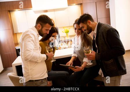 Groupe de jeunes heureux préparant des repas, à la recherche de recettes à la tablette numérique, boire du vin blanc et passer un bon moment Banque D'Images