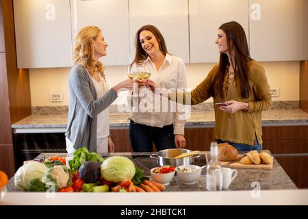 Groupe de jolies jeunes femmes préparant un repas, buvant du vin blanc et ayant un bon moment Banque D'Images