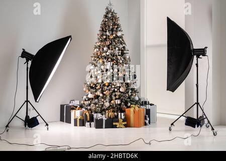 Sapin de Noël en studio photo intérieur blanc avec élégant coffret cadeau noir et orange debout comme modèle de mode avec flash équipement Banque D'Images