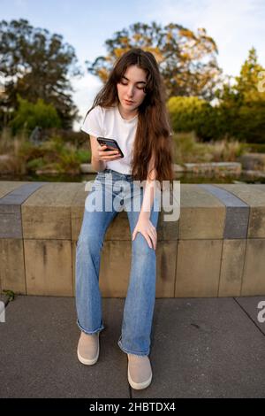 Une adolescente utilisant son smartphone par un étang rempli de Lilly Banque D'Images