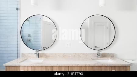 Une longue salle de bains meuble-lavabo en bois avec comptoirs en granit, miroirs circulaires, lampes suspendues au plafond, avec vue sur la douche carrelée de bleu. Banque D'Images