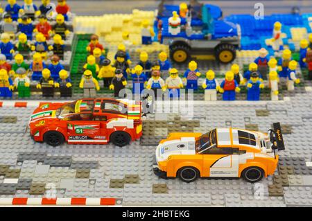 POZNAN, POLOGNE - 28 avril 2018 : deux voitures de course Lego sur une piste et de nombreux personnages de jouets spectateurs regardant la compétition Banque D'Images