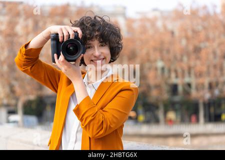 Jeune femme brunette avec des cheveux bouclés prenant une photo regardant l'appareil photo Banque D'Images