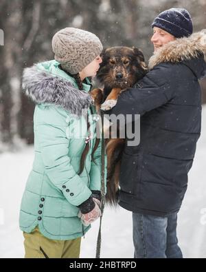 Joyeux jeune couple marchant avec un chien dans la forêt le jour d'hiver Banque D'Images