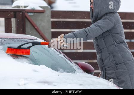 Une jeune femme se brosser la neige de la voiture après une forte chute de neige Banque D'Images