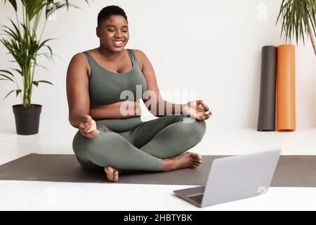 Belle femme noire chubby s'exerçant à la maison, à l'aide d'un ordinateur portable Banque D'Images