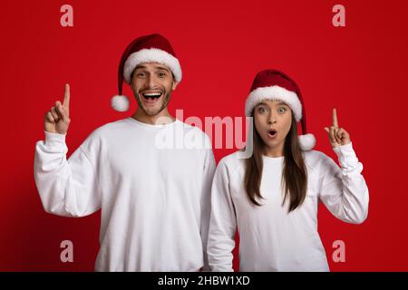 Idées de Noël.Joyeux jeune couple à Santa Hats pointant les doigts de l'index vers le haut Banque D'Images