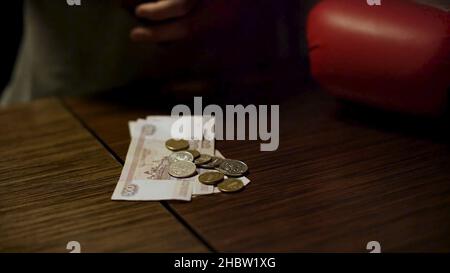 Gros plan des mains d'homme tenant un portefeuille en cuir ouvert avec quelques pièces à l'intérieur sur une vieille table en bois avec de l'argent en papier couché sur elle.Pièces de mise mâles Banque D'Images